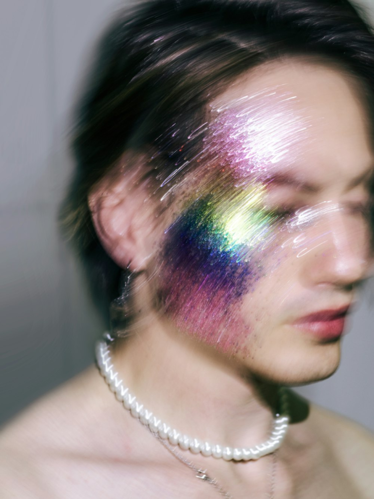 A man with a multicolored face and a pearl necklace, symbolizing artistic expression, diversity, and individuality.
