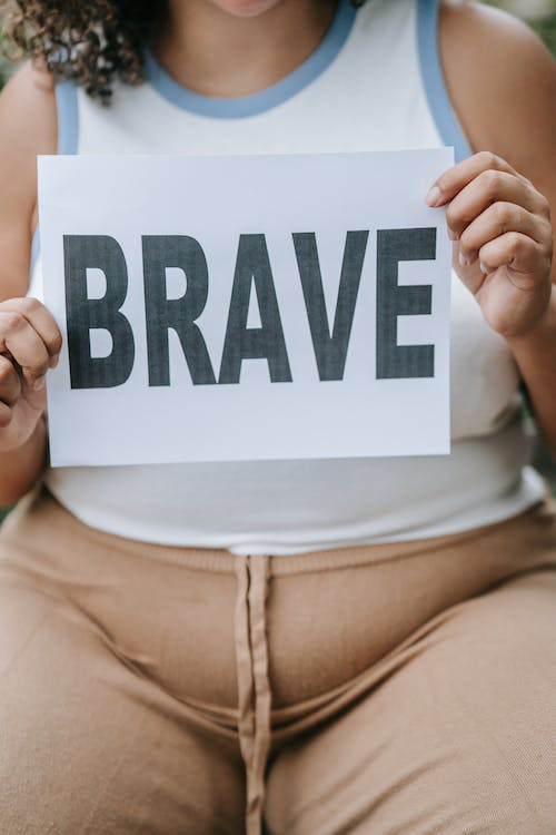 Woman holding a paper with "brave" written on it